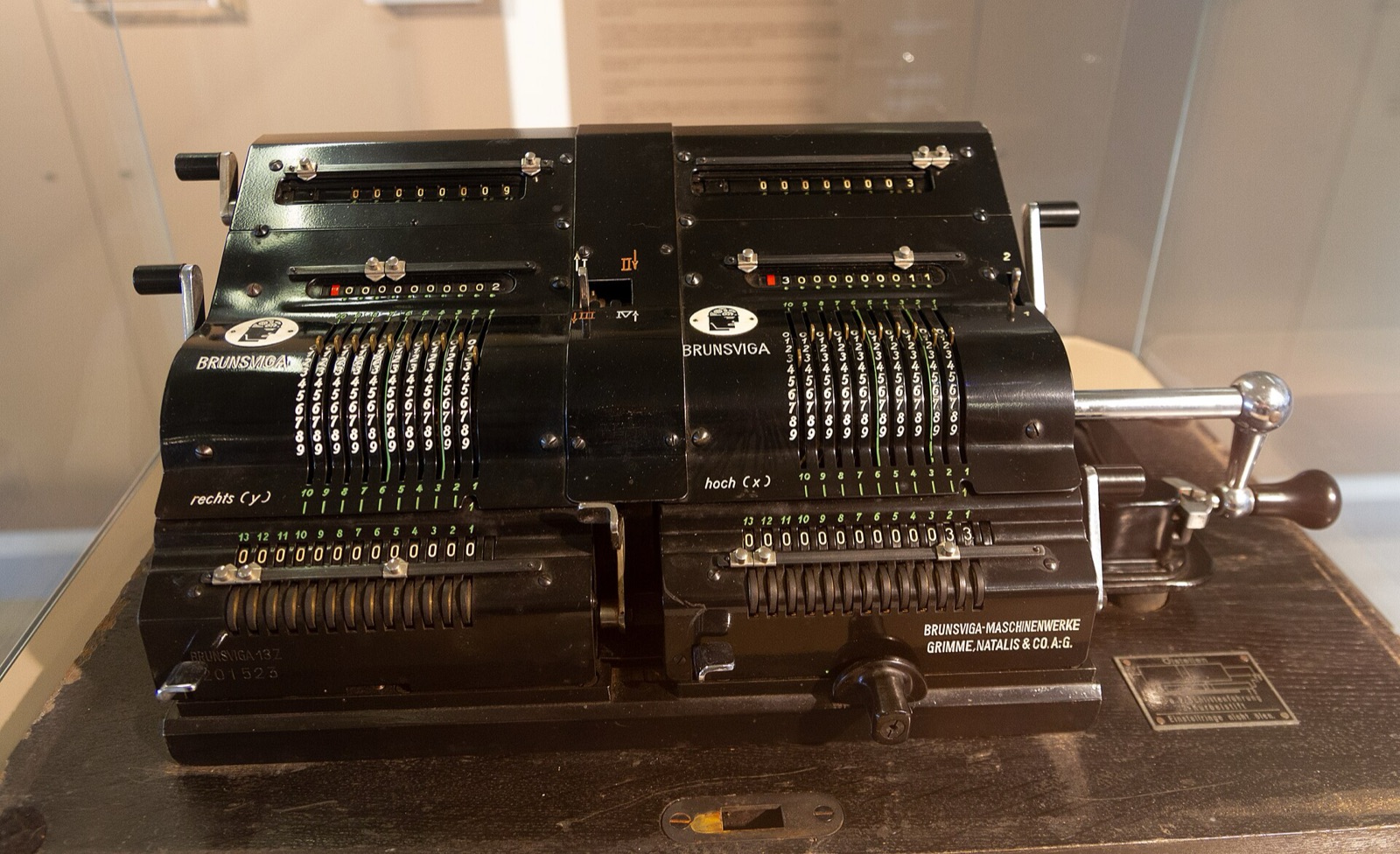 Une calculatrice mécanique Brunsviga noire, avec ses curseurs à chiffres et sa manivelle, posée dans une vitrine de musée